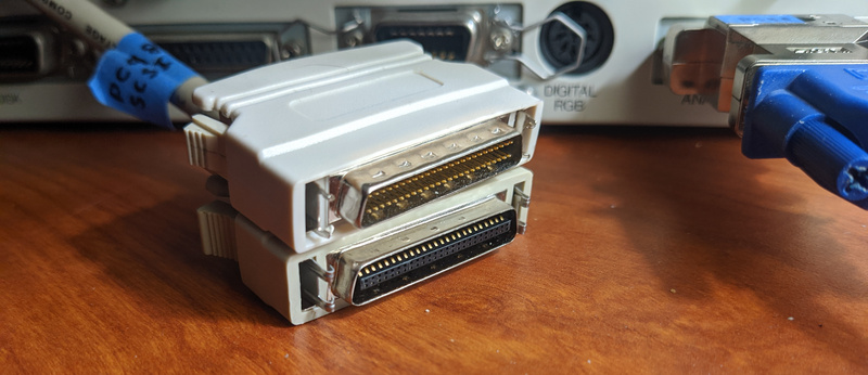 (Picture of a so-called mini centronics male connector for SCSI drives, with an HD50 male SCSI terminator on top of it for visual comparison)